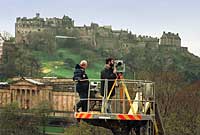 Two people, high on a crane, taking a photogrammetric survey of the Monument, with the castle in the background.